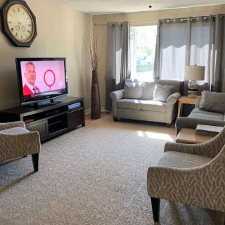 A cozy living room featuring a sofa, armchairs, a television, and large windows with natural light.