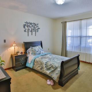 A cozy bedroom with a single bed and a nightstand, softly lit by a lamp.
