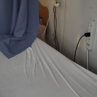 A hospital bed with a sheet and curtain, showing an electrical outlet in the background.