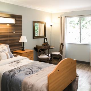 A modern and cozy bedroom with a wooden bed, desk, and natural light from the window.