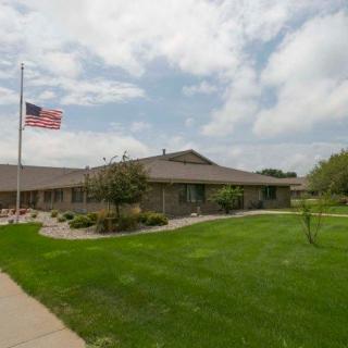 A single-story building with a well-maintained lawn and an American flag waving on a flagpole under a partly cloudy sky.