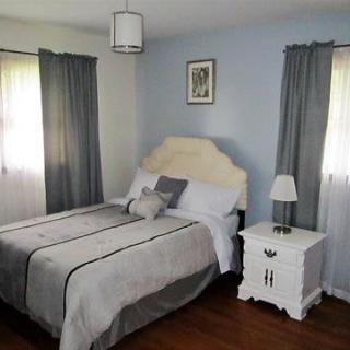 A cozy bedroom with a neatly made bed, soft gray curtains, and a white nightstand with a lamp.