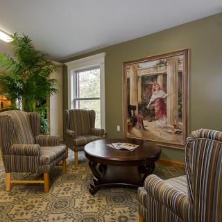 A cozy living room with four striped armchairs, a central wooden coffee table, a large painting on the wall, and a decorative plant by the window.