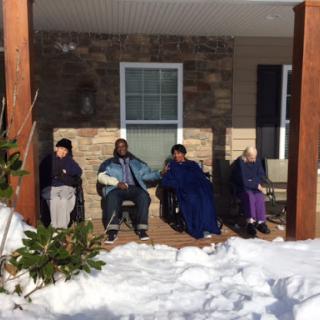 A group of individuals enjoying a sunny winter day on the porch, surrounded by snow.