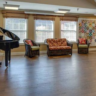 A cozy living room with a piano, comfortable seating, and large windows.
