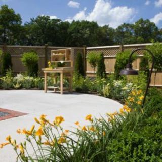 A beautifully landscaped garden featuring bright yellow daylilies and lush greenery, enclosed by a wooden fence.