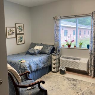 A cozy and well-decorated bedroom with a bed, chair, and indoor plants by the window.