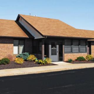 A small brick office building with a sloped roof and landscaped surroundings.