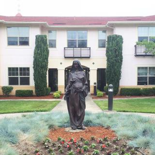 A statue in front of a two-story building with well-maintained gardens.