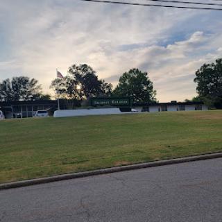 A serene view of a grassy area surrounded by trees under a partly cloudy sky.