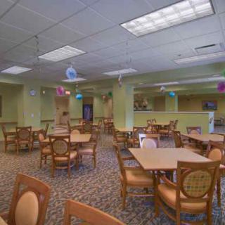 An empty dining area with chairs and tables arranged on a carpeted floor and ceiling lights overhead.