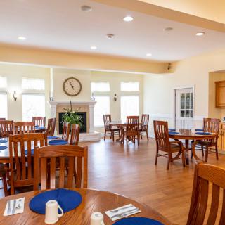 A spacious and well-lit dining room with wooden tables and chairs, decorated with a clock on the wall.