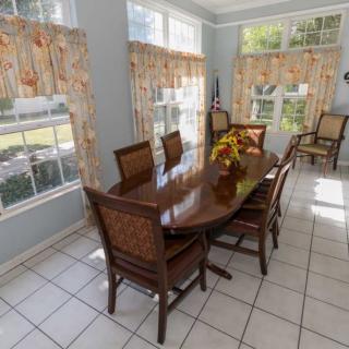 A bright dining room with a wooden table, chairs, and large windows adorned with patterned curtains.
