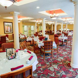 An elegantly decorated dining room with neatly arranged tables and chairs, featuring chandeliers and a patterned carpet.