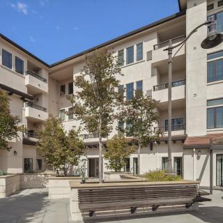 A modern apartment building with a landscaped courtyard featuring trees and benches.