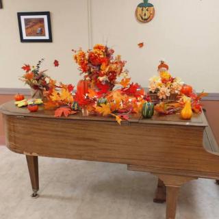 A piano decorated with vibrant autumn-themed arrangements, featuring leaves and gourds.