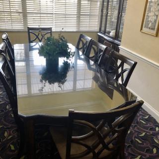 A dining room with a large table and eight chairs, featuring floral centerpiece decor and window blinds.