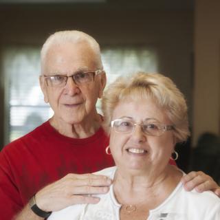 An elderly couple smiling and posing together indoors.