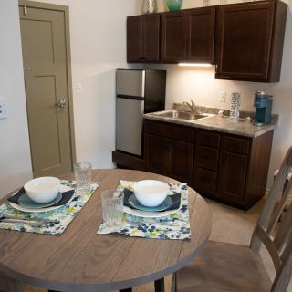 A cozy kitchen and dining area with a table set for two, featuring dark wood cabinets and a small refrigerator.