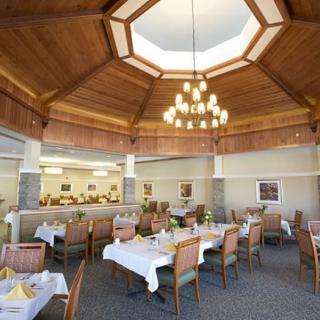 A well-lit restaurant interior with a stylish chandelier, featuring neatly arranged tables and chairs under a wooden ceiling.