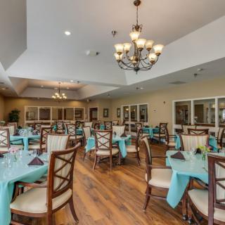 A spacious dining room with neatly arranged tables, turquoise tablecloths, and elegant chandeliers.