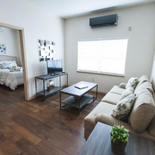 A modern living room with a cozy sofa, coffee table, and television, leading into a bedroom.
