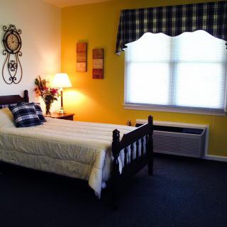 A cozy bedroom with a wooden bed, yellow accent wall, and a window adorned with a checkered valance.