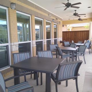 A covered outdoor patio with tables and chairs, featuring ceiling fans for comfort.