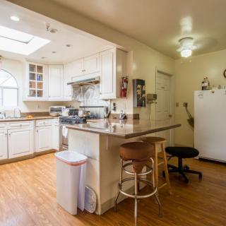 A modern kitchen interior with white cabinets and wood flooring, featuring a large countertop with bar stools.
