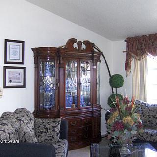 A living room with a decorative cabinet, floral arrangement, and natural lighting.