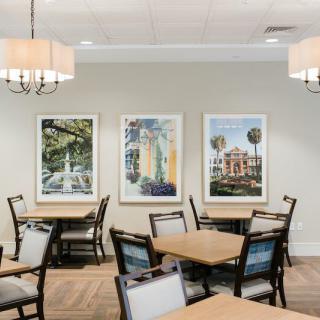 A modern dining area with tables and chairs, featuring artwork on the walls and elegant lighting fixtures.