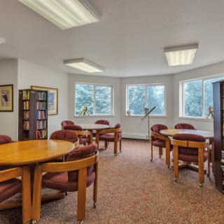 A quiet library reading room with tables and chairs, illuminated by natural light from the windows.