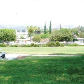 A scenic view of a park with grass, trees, and distant hills.