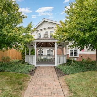 A charming house featuring a gazebo surrounded by lush greenery and a brick pathway.