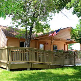 A cozy home featuring a wooden deck, surrounded by greenery and an American flag.