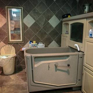 A bathroom featuring a large walk-in bathtub and tiled walls, with a mirror and storage cabinet.