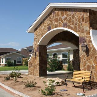 A stone archway entrance with a bench, leading to residential buildings and landscaped gardens.