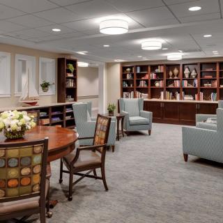 A cozy interior space featuring a seating area with armchairs, bookshelves filled with books, and a central table.