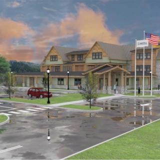 A hospital building with flags and a parking area under a cloudy sky.