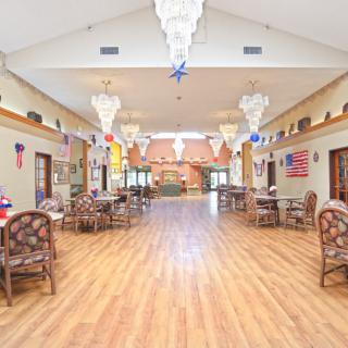 A spacious hall with chandeliers, wood flooring, and arranged tables and chairs.