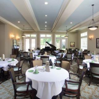 An elegant dining room with tables set for a meal and a piano in the background.
