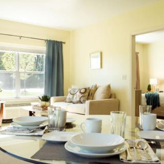 A cozy dining area with a set table, adjacent to a bright and inviting living room.