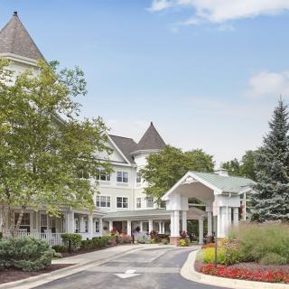 A large building with an elegant entrance, surrounded by trees and landscaping under a clear sky.