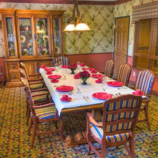 A cozy dining room with a table set for a meal, featuring wooden chairs, a china cabinet, and a warm chandelier.