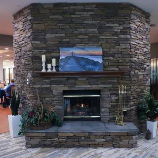 A cozy stone fireplace with decorative candles, plants, and artwork in a living room setting.