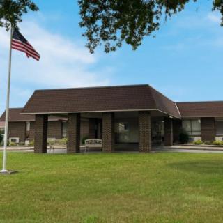 A single-story brick building with an American flag on the lawn under a clear blue sky.