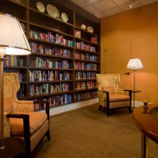 A cozy library room with bookshelves, armchairs, and lamps for reading.