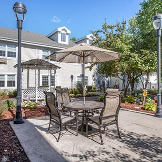 A cozy outdoor patio area with tables and chairs under umbrellas, surrounded by a well-maintained garden in a residential setting.