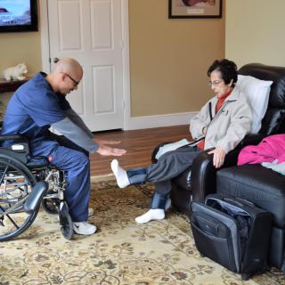 A caregiver assists a person with leg exercises in a home setting.