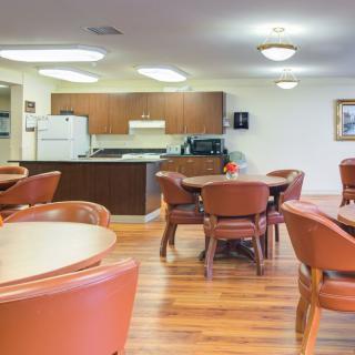 A well-lit kitchen and dining area with multiple tables and chairs, featuring a hardwood floor.